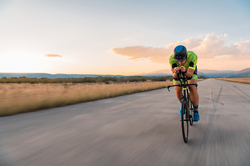 Image showing Triathlete riding his bicycle during sunset, preparing for a marathon. The warm colors of the sky provide a beautiful backdrop for his determined and focused effort.