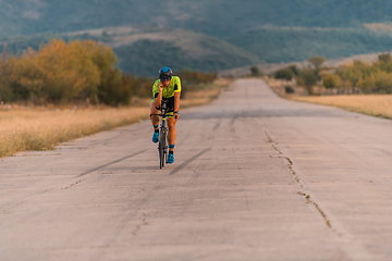 Image showing Triathlete riding his bicycle during sunset, preparing for a marathon. The warm colors of the sky provide a beautiful backdrop for his determined and focused effort.