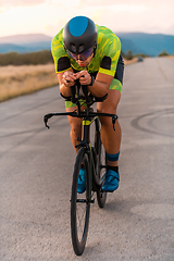 Image showing Triathlete riding his bicycle during sunset, preparing for a marathon. The warm colors of the sky provide a beautiful backdrop for his determined and focused effort.