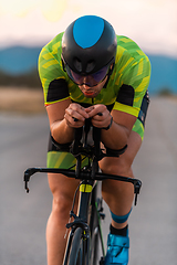 Image showing Close up photo of triathlete riding his bicycle during sunset, preparing for a marathon. The warm colors of the sky provide a beautiful backdrop for his determined and focused effort.