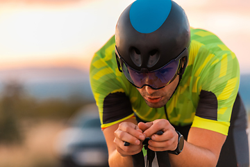 Image showing Close up photo of triathlete riding his bicycle during sunset, preparing for a marathon. The warm colors of the sky provide a beautiful backdrop for his determined and focused effort.