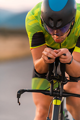 Image showing Close up photo of triathlete riding his bicycle during sunset, preparing for a marathon. The warm colors of the sky provide a beautiful backdrop for his determined and focused effort.