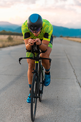 Image showing Triathlete riding his bicycle during sunset, preparing for a marathon. The warm colors of the sky provide a beautiful backdrop for his determined and focused effort.