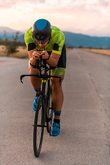 Image showing Triathlete riding his bicycle during sunset, preparing for a marathon. The warm colors of the sky provide a beautiful backdrop for his determined and focused effort.