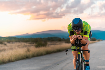 Image showing Triathlete riding his bicycle during sunset, preparing for a marathon. The warm colors of the sky provide a beautiful backdrop for his determined and focused effort.