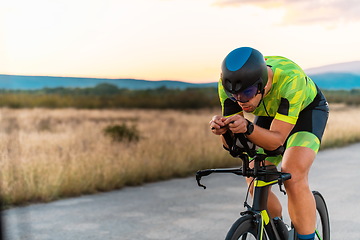 Image showing Triathlete riding his bicycle during sunset, preparing for a marathon. The warm colors of the sky provide a beautiful backdrop for his determined and focused effort.