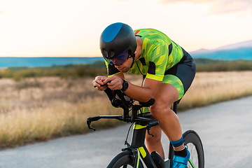 Image showing Close up photo of triathlete riding his bicycle during sunset, preparing for a marathon. The warm colors of the sky provide a beautiful backdrop for his determined and focused effort.