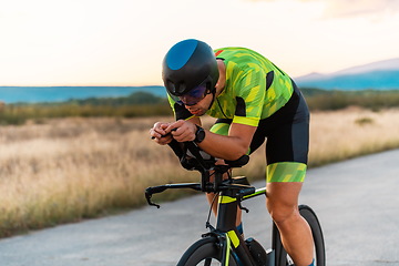 Image showing Triathlete riding his bicycle during sunset, preparing for a marathon. The warm colors of the sky provide a beautiful backdrop for his determined and focused effort.