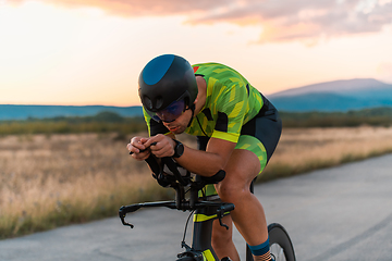 Image showing Close up photo of triathlete riding his bicycle during sunset, preparing for a marathon. The warm colors of the sky provide a beautiful backdrop for his determined and focused effort.