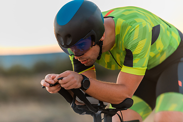 Image showing Close up photo of triathlete riding his bicycle during sunset, preparing for a marathon. The warm colors of the sky provide a beautiful backdrop for his determined and focused effort.