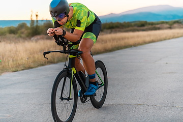 Image showing Triathlete riding his bicycle during sunset, preparing for a marathon. The warm colors of the sky provide a beautiful backdrop for his determined and focused effort.