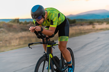 Image showing Close up photo of triathlete riding his bicycle during sunset, preparing for a marathon. The warm colors of the sky provide a beautiful backdrop for his determined and focused effort.