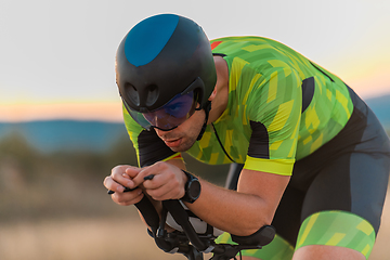 Image showing Close up photo of triathlete riding his bicycle during sunset, preparing for a marathon. The warm colors of the sky provide a beautiful backdrop for his determined and focused effort.