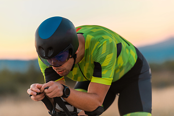 Image showing Close up photo of triathlete riding his bicycle during sunset, preparing for a marathon. The warm colors of the sky provide a beautiful backdrop for his determined and focused effort.