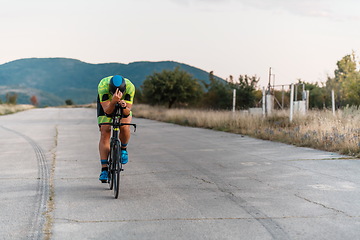 Image showing Triathlete riding his bicycle during sunset, preparing for a marathon. The warm colors of the sky provide a beautiful backdrop for his determined and focused effort.