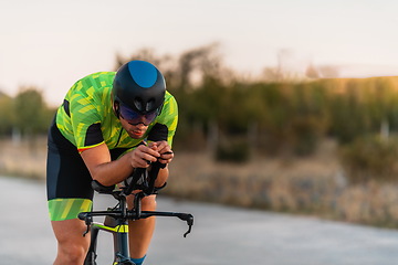 Image showing Triathlete riding his bicycle during sunset, preparing for a marathon. The warm colors of the sky provide a beautiful backdrop for his determined and focused effort.