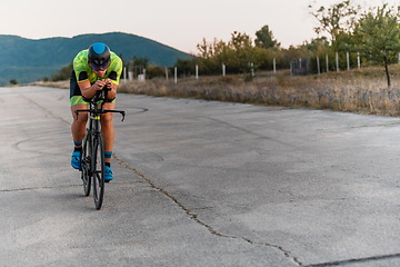 Image showing Triathlete riding his bicycle during sunset, preparing for a marathon. The warm colors of the sky provide a beautiful backdrop for his determined and focused effort.