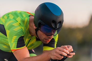 Image showing Close up photo of triathlete riding his bicycle during sunset, preparing for a marathon. The warm colors of the sky provide a beautiful backdrop for his determined and focused effort.