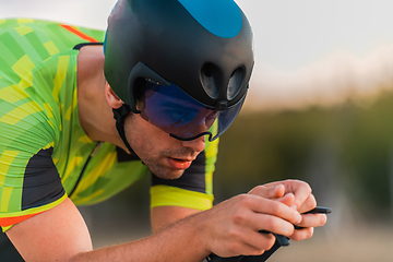 Image showing Close up photo of triathlete riding his bicycle during sunset, preparing for a marathon. The warm colors of the sky provide a beautiful backdrop for his determined and focused effort.