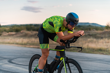 Image showing Triathlete riding his bicycle during sunset, preparing for a marathon. The warm colors of the sky provide a beautiful backdrop for his determined and focused effort.