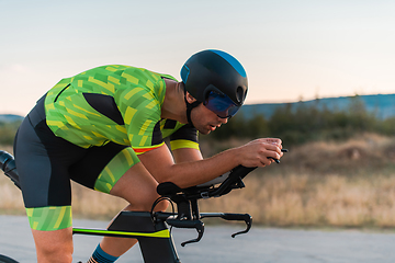 Image showing Close up photo of triathlete riding his bicycle during sunset, preparing for a marathon. The warm colors of the sky provide a beautiful backdrop for his determined and focused effort.