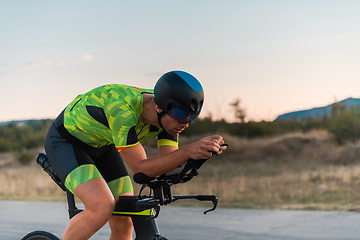 Image showing Triathlete riding his bicycle during sunset, preparing for a marathon. The warm colors of the sky provide a beautiful backdrop for his determined and focused effort.