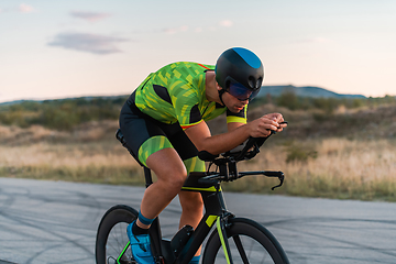 Image showing Triathlete riding his bicycle during sunset, preparing for a marathon. The warm colors of the sky provide a beautiful backdrop for his determined and focused effort.