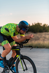 Image showing Triathlete riding his bicycle during sunset, preparing for a marathon. The warm colors of the sky provide a beautiful backdrop for his determined and focused effort.