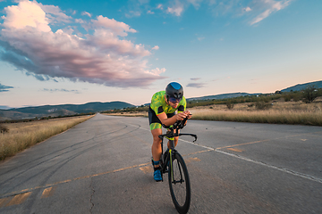 Image showing Triathlete riding his bicycle during sunset, preparing for a marathon. The warm colors of the sky provide a beautiful backdrop for his determined and focused effort.