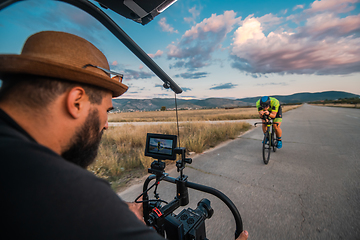 Image showing A videographer recording a triathlete riding his bike preparing for an upcoming marathon.Athlete's physical endurance and the dedication required to succeed in the sport.