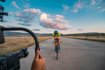 Image showing A videographer recording a triathlete riding his bike preparing for an upcoming marathon.Athlete's physical endurance and the dedication required to succeed in the sport.