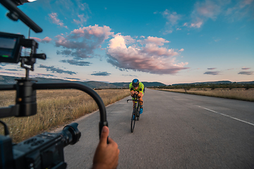 Image showing A videographer recording a triathlete riding his bike preparing for an upcoming marathon.Athlete's physical endurance and the dedication required to succeed in the sport.