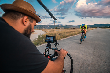 Image showing A videographer recording a triathlete riding his bike preparing for an upcoming marathon.Athlete's physical endurance and the dedication required to succeed in the sport.