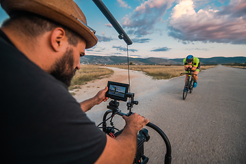 Image showing A videographer recording a triathlete riding his bike preparing for an upcoming marathon.Athlete's physical endurance and the dedication required to succeed in the sport.