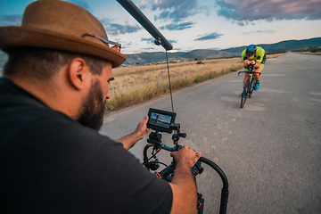 Image showing A videographer recording a triathlete riding his bike preparing for an upcoming marathon.Athlete's physical endurance and the dedication required to succeed in the sport.