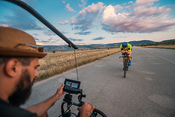 Image showing A videographer recording a triathlete riding his bike preparing for an upcoming marathon.Athlete's physical endurance and the dedication required to succeed in the sport.