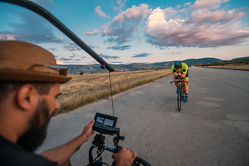 Image showing A videographer recording a triathlete riding his bike preparing for an upcoming marathon.Athlete's physical endurance and the dedication required to succeed in the sport.