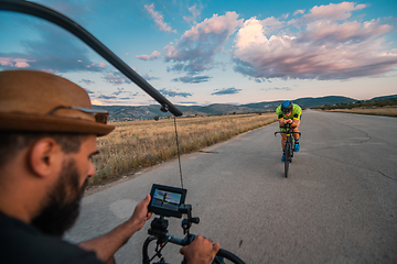 Image showing A videographer recording a triathlete riding his bike preparing for an upcoming marathon.Athlete's physical endurance and the dedication required to succeed in the sport.