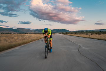 Image showing Triathlete riding his bicycle during sunset, preparing for a marathon. The warm colors of the sky provide a beautiful backdrop for his determined and focused effort.