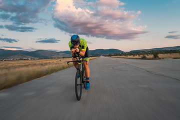 Image showing Triathlete riding his bicycle during sunset, preparing for a marathon. The warm colors of the sky provide a beautiful backdrop for his determined and focused effort.