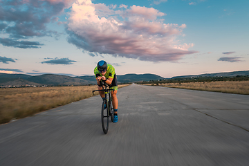 Image showing Triathlete riding his bicycle during sunset, preparing for a marathon. The warm colors of the sky provide a beautiful backdrop for his determined and focused effort.