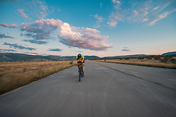 Image showing Triathlete riding his bicycle during sunset, preparing for a marathon. The warm colors of the sky provide a beautiful backdrop for his determined and focused effort.