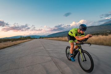 Image showing Triathlete riding his bicycle during sunset, preparing for a marathon. The warm colors of the sky provide a beautiful backdrop for his determined and focused effort.