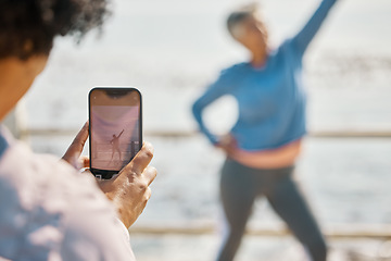 Image showing Phone, fitness and photograph of woman at beach in silly pose at sea for senior friends. Exercise, mobile and picture for social media post on a ocean promenade walk for nature workout and friendship