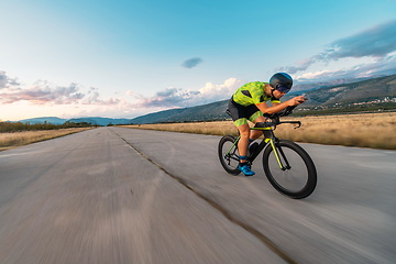 Image showing Triathlete riding his bicycle during sunset, preparing for a marathon. The warm colors of the sky provide a beautiful backdrop for his determined and focused effort.