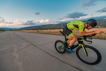 Image showing Triathlete riding his bicycle during sunset, preparing for a marathon. The warm colors of the sky provide a beautiful backdrop for his determined and focused effort.