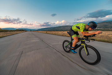 Image showing Triathlete riding his bicycle during sunset, preparing for a marathon. The warm colors of the sky provide a beautiful backdrop for his determined and focused effort.