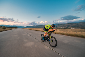 Image showing Triathlete riding his bicycle during sunset, preparing for a marathon. The warm colors of the sky provide a beautiful backdrop for his determined and focused effort.