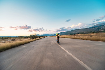 Image showing Triathlete riding his bicycle during sunset, preparing for a marathon. The warm colors of the sky provide a beautiful backdrop for his determined and focused effort.