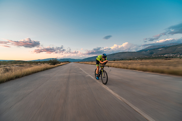 Image showing Triathlete riding his bicycle during sunset, preparing for a marathon. The warm colors of the sky provide a beautiful backdrop for his determined and focused effort.